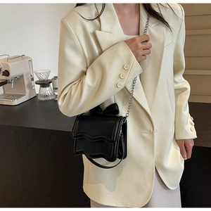 Close-up of black glossy leather mini bag with bow decoration and silver chain strap