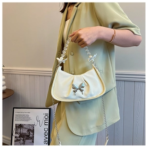 Detail of white pleated handbag with pearl handle and silver butterfly charm on model