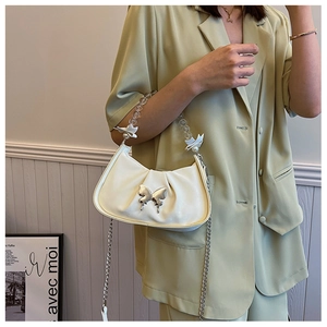 Detail of cream pleated crescent bag featuring silver butterfly and pearl bead handle