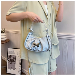 Detail of silver pleated handbag with golden butterfly clasp and pearl bead handle