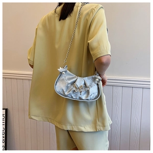 Detail of silver pleated shoulder bag featuring beaded handle and metal bow accents