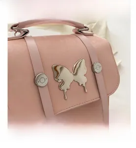 Close-up of pink shoulder bag featuring a large silver metal butterfly and strap details