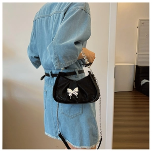 Detail of black saddle bag featuring silver butterfly buckle and pearl beaded handle