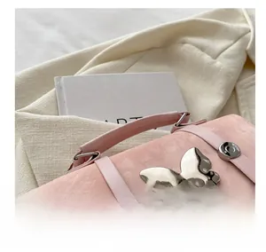 Detail shot of a pink suede handbag featuring a large mirror-finish metal butterfly buckle