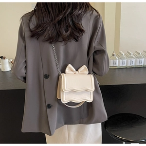 Detail of cream crossbody bag with bow decoration and scalloped edges on silver chain