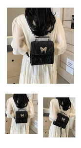 Detail view of black textured PU leather backpack with a large silver metal butterfly charm