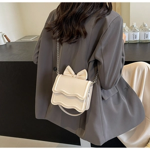 Detail of cream white crossbody bag with wave flap and decorative bow on grey blazer