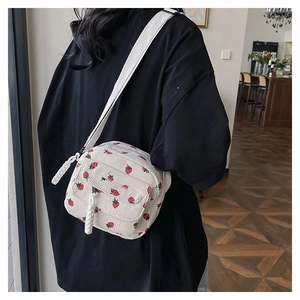 Detail view of white corduroy crossbody bag with cute red strawberry patterns on a strap