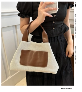 Detail view of a beige woven bucket bag with brown leather handles on a black dress