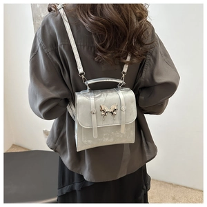 Detail of silver metallic mini backpack with butterfly buckle on model's back
