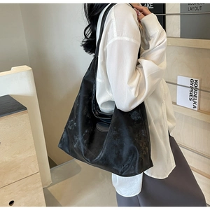 Gros plan du sac cabas noir mat texturé porté par un mannequin en chemise blanche