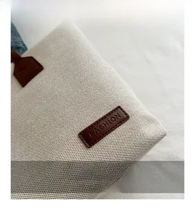 Close-up of beige canvas tote bag with a brown leather patch and Fashion engraving