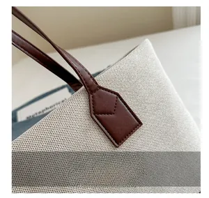 Detail view of beige canvas tote with brown leather handles and reinforced stitching