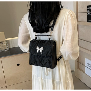 Detail of black pleated nylon backpack featuring a silver butterfly metal buckle