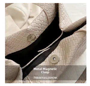 Detail of metal magnetic buckle closure on cream woven leather handbag with black lining