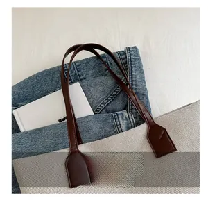 Close-up of reinforced brown leather straps on a vintage canvas tote bag with soft lighting