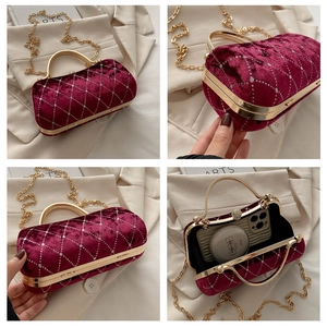 Macro detail of burgundy velvet evening bag with rhinestone quilting and gold metal handle