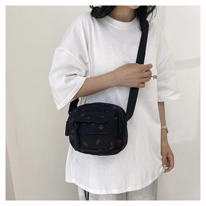 Close-up of black corduroy crossbody bag with cute strawberry pattern and nylon strap