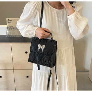 Detail of black pleated fabric and silver butterfly ornament on stylish handbag