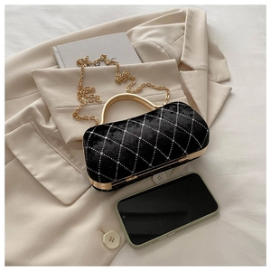 Detail of black velvet clutch bag with diamond quilting and gold handle on a beige blazer