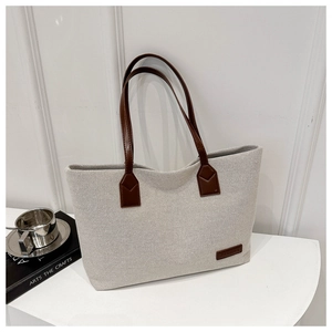 Detail of beige canvas tote bag showing brown leather handles and fashion letter patch