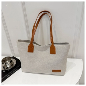 Detail of the minimalist canvas tote bag with brown leather logo patch and stitched handles