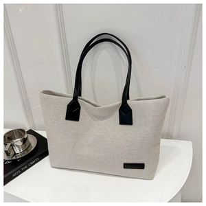 Detail of cream canvas tote bag with black leather handles and fashion logo tag