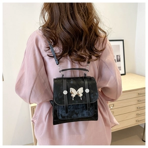 Close-up of black velvet backpack featuring silver butterfly accent and leather straps
