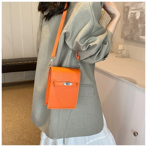 Détail du sac bandoulière en cuir orange avec fermoir rotatif argenté porté par un mannequin