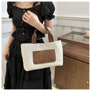 Detail of canvas tote bag featuring brown leather handles and a front pocket design