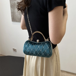 Model wearing a velvet crossbody bag with golden handle and pearl clasp detail