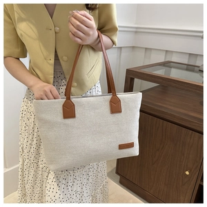 Detail of canvas tote bag with brown leather handles held by model in yellow blazer