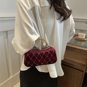 Detail of burgundy velvet clutch bag with quilted pattern and metal handle on model