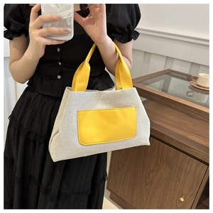 Detail of canvas tote bag with contrast yellow leather handles and front pocket