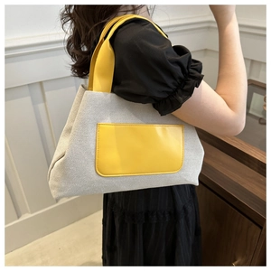 Detail of canvas tote bag with yellow leather straps shown on a model's shoulder