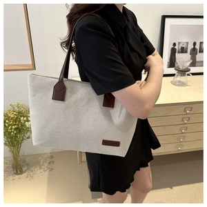 Detail view of large canvas tote bag with brown leather straps and patch logo