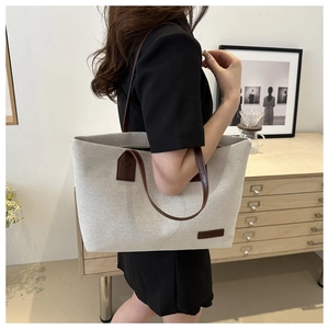 Close-up of beige canvas tote with brown leather straps and reinforced stitching detail