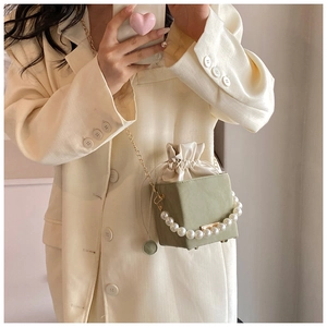 Détail du sac seau vert clair avec anse en perles et chaîne dorée sur blazer beige