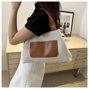 Detail of cream woven tote bag with a brown leather pocket and handle on a model
