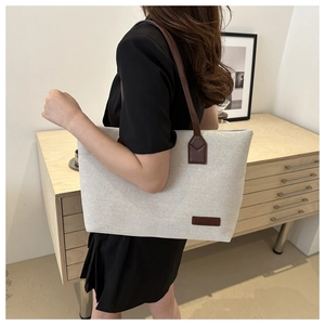 Close-up of a large canvas tote bag with brown leather handles and a fashion logo patch