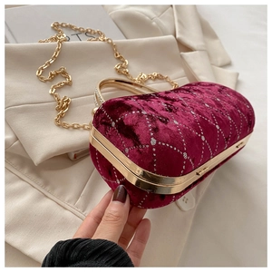 Close-up of velvet handbag with burgundy diamond pattern and gold chain handle