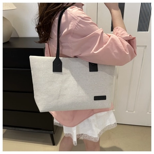 Detail of off-white canvas tote bag with long black leather straps and fashion label