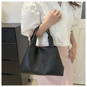 Detalle de la textura tejida de un bolso tote negro minimalista llevado por una modelo real