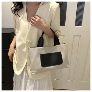 Close-up of beige canvas bucket bag with black leather handle and front pocket detail