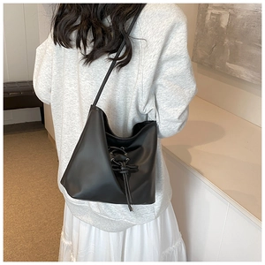 Détail du sac seau en cuir noir avec cordon à nœud porté par un mannequin femme