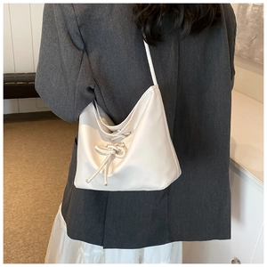 Chic cream bucket bag with bow detail worn over the shoulder on a modern grey suit