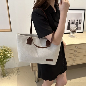 Minimalist canvas tote bag with brown leather straps shown on shoulder in home setting