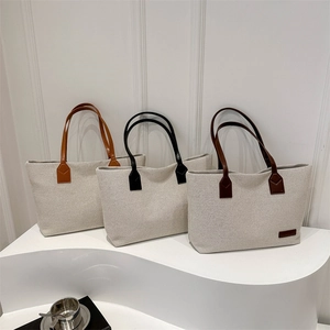 Three canvas tote bags with colorful leather straps displayed on a minimalist white stand