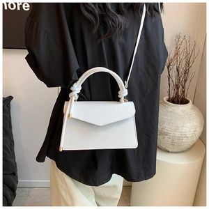 Close-up of white lychee pattern leather handbag with knotted handle and metal details