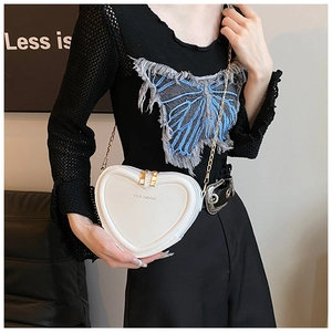 Detailaufnahme einer weißen herzförmigen Umhängetasche mit goldener Kette getragen am Model